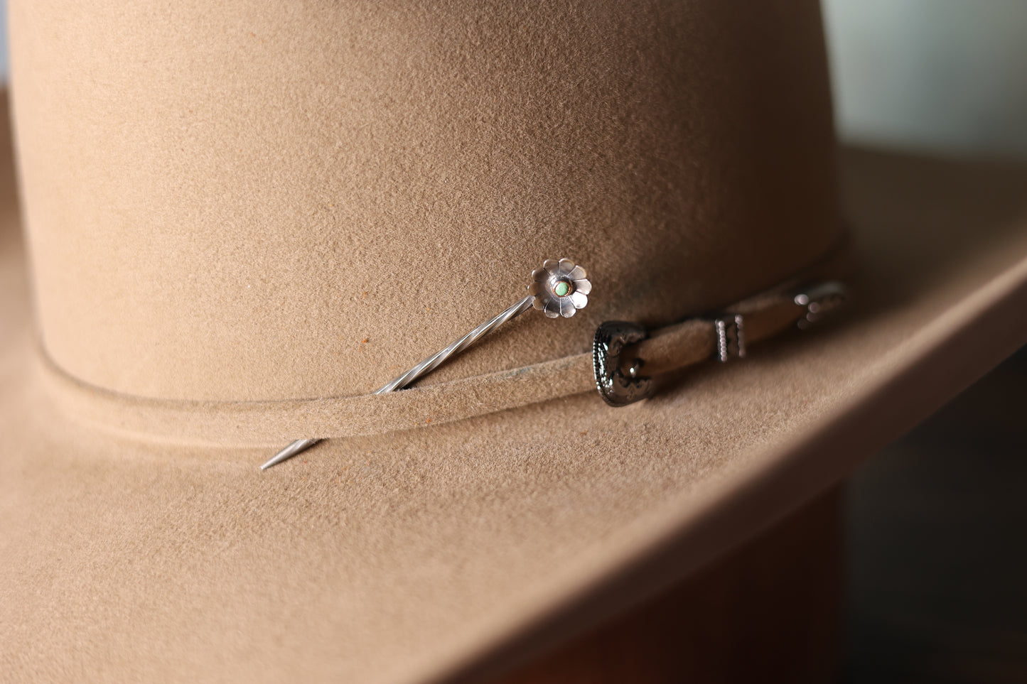 Photo of the gold flower metal tooth pick from Greeley Hat Works, inserted in a tan cowboy hat