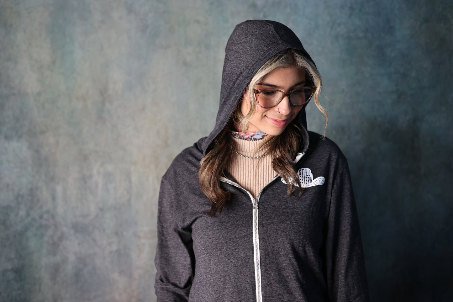 Photo of woman wearing grey Still Western Zip-up Hoodie from Greeley Hat works with the hood up