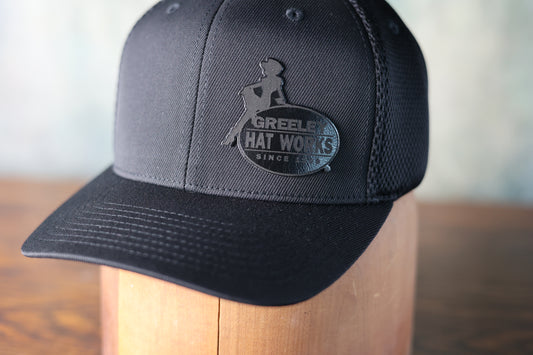 Close-up photo of the new black leather patch baseball hat from Greeley Hat Works with the logo in black on black