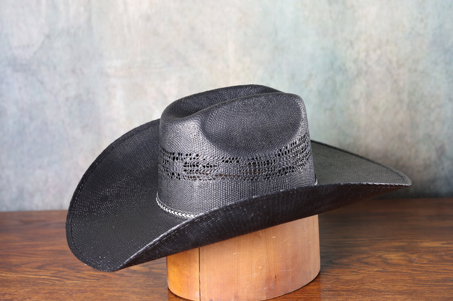 Photo of the side of a Black Bangora Pre-Shape 4 1/2” Brim cowboy hat on a wooden block with a textured gray background