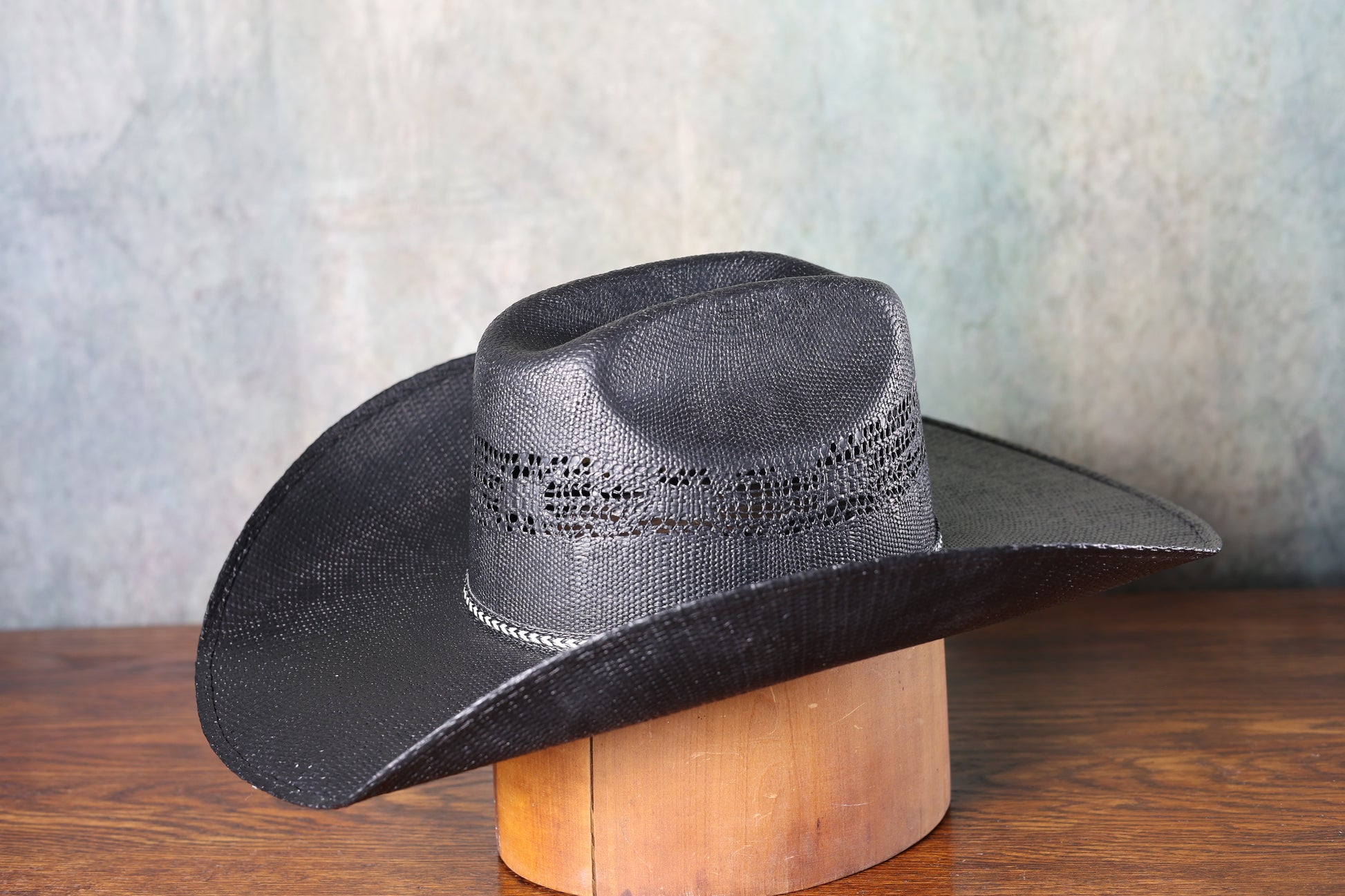 Photo of the side of a Black Bangora Pre-Shape 4 1/2” Brim cowboy hat on a wooden block with a textured gray background