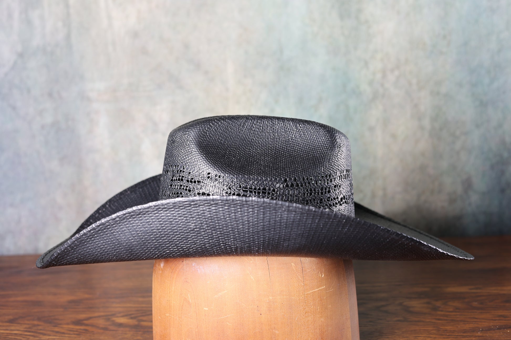 Photo of the side of the black Bangora Pre-Shape 4 1/2” Brim cowboy hat on a wooden block with a textured gray background