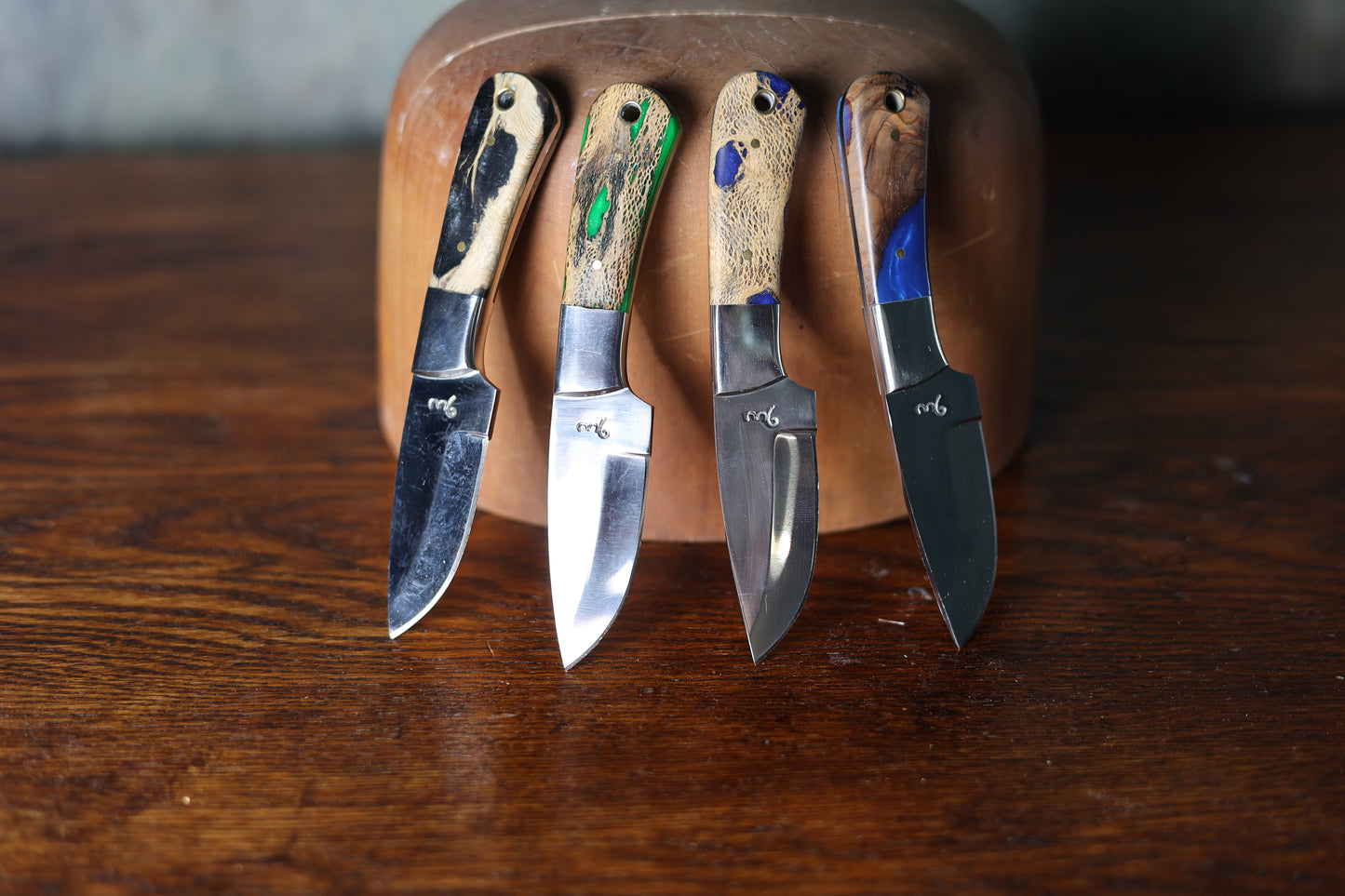 Four 9 Lazy 3 Knives with different handles on a wooden hat block against a dark background