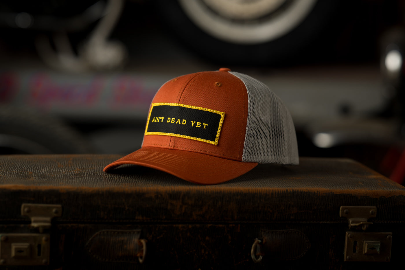 Photo of orange Ain’t Dead Yet Cap from Greeley Hat Works on an antique trunk