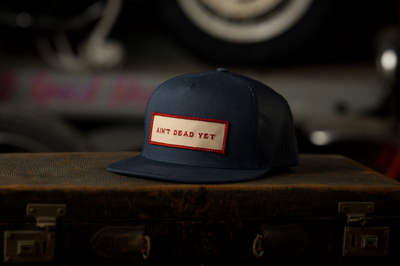 Photo of navy blue Ain’t Dead Yet Cap from Greeley Hat Works on antique trunk